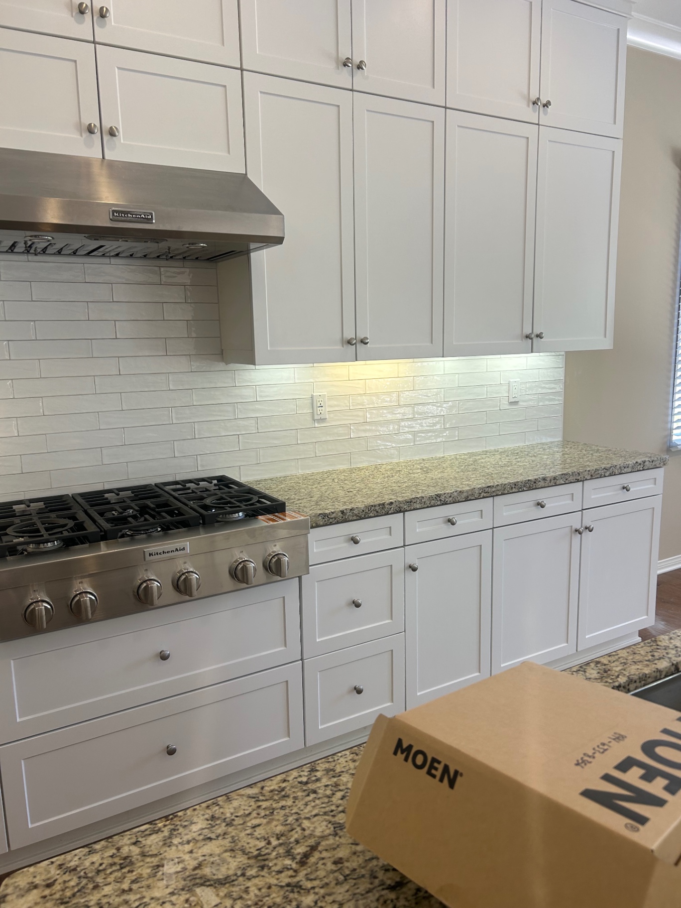 White kitchen with glossy handmade subway backsplash, KitchenAid range and stainless hood