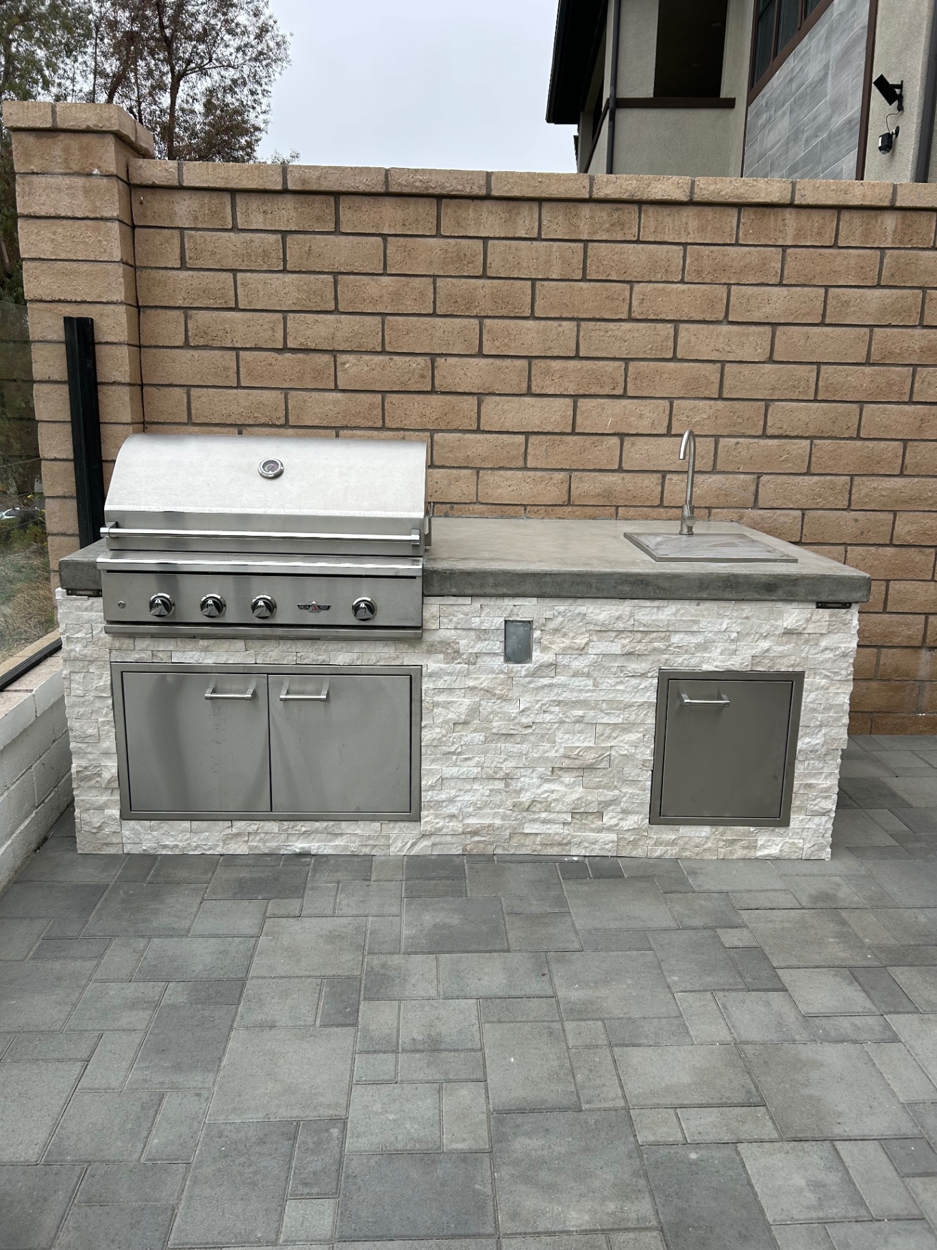Built-in outdoor kitchen with white stacked stone, concrete counter and grill
