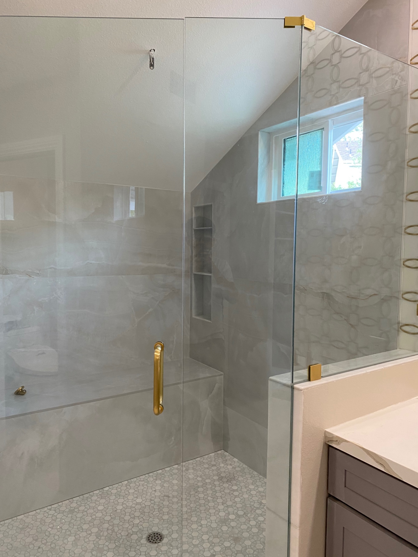 Onyx-look porcelain walk-in shower with gold hardware, bench and pebble floor