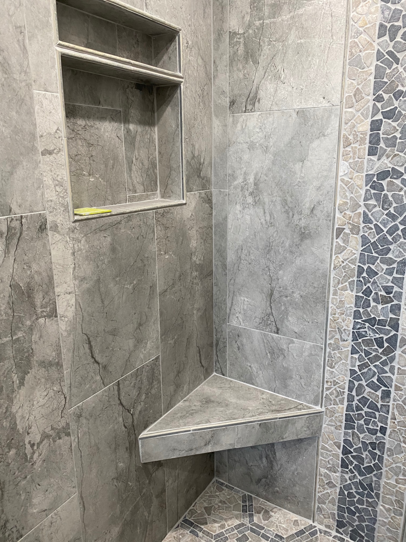 Gray marble shower bench and double niche with pebble mosaic accent