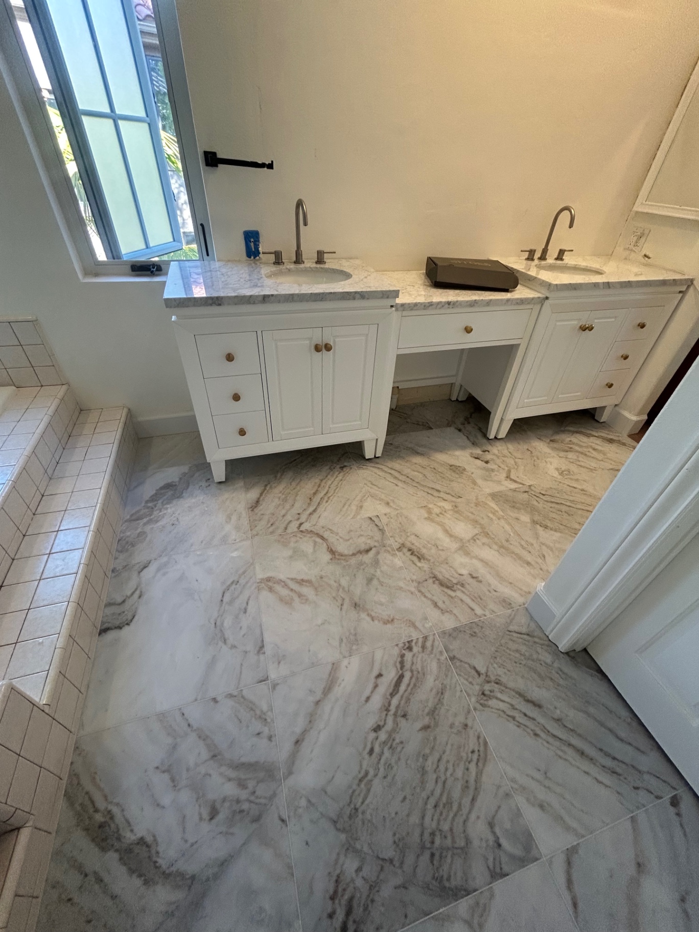 Double white vanity with Carrara marble tops over large-format marble-look floor tile