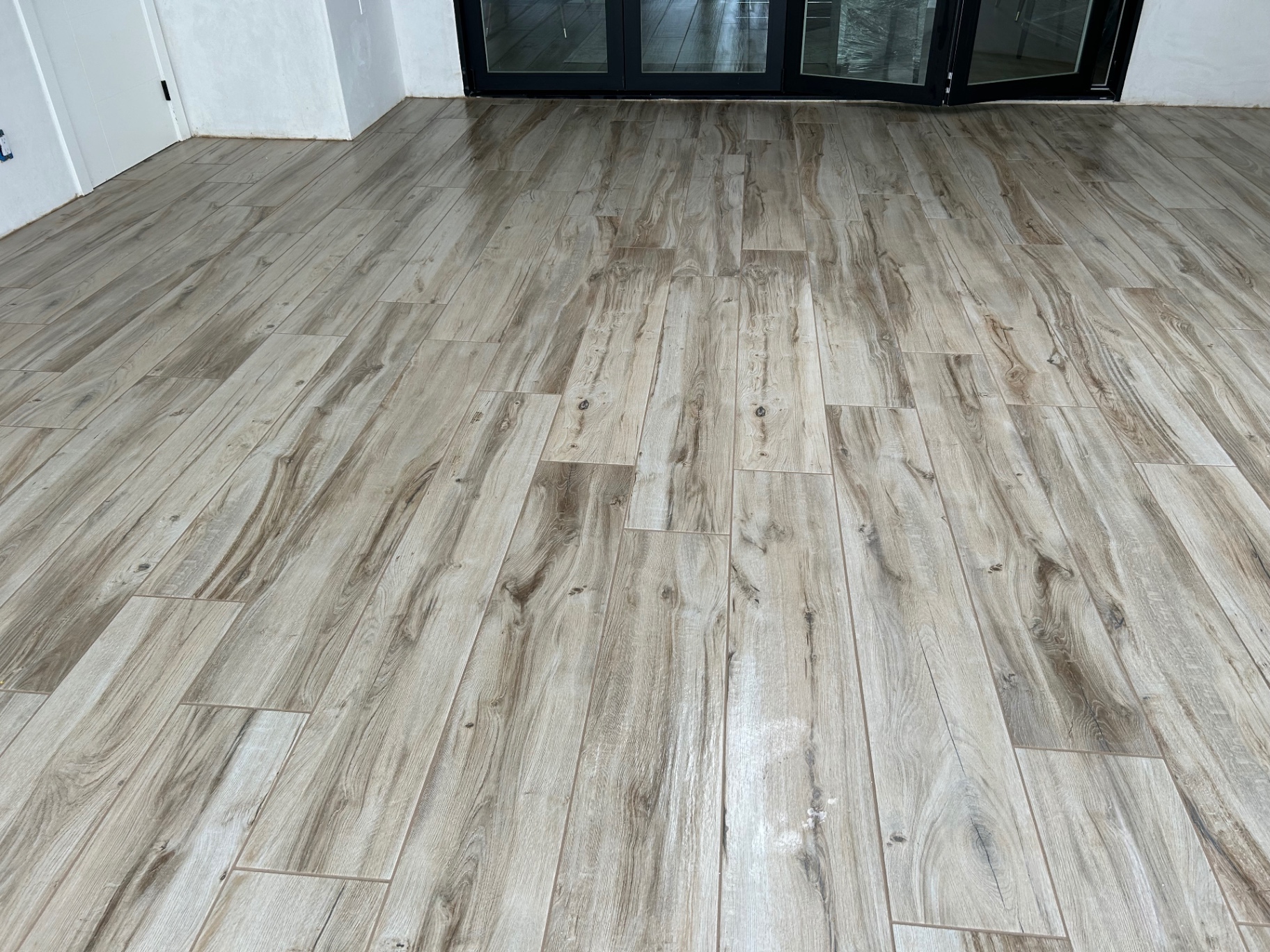 Wide wood-plank porcelain tile floor in living area with black bifold doors