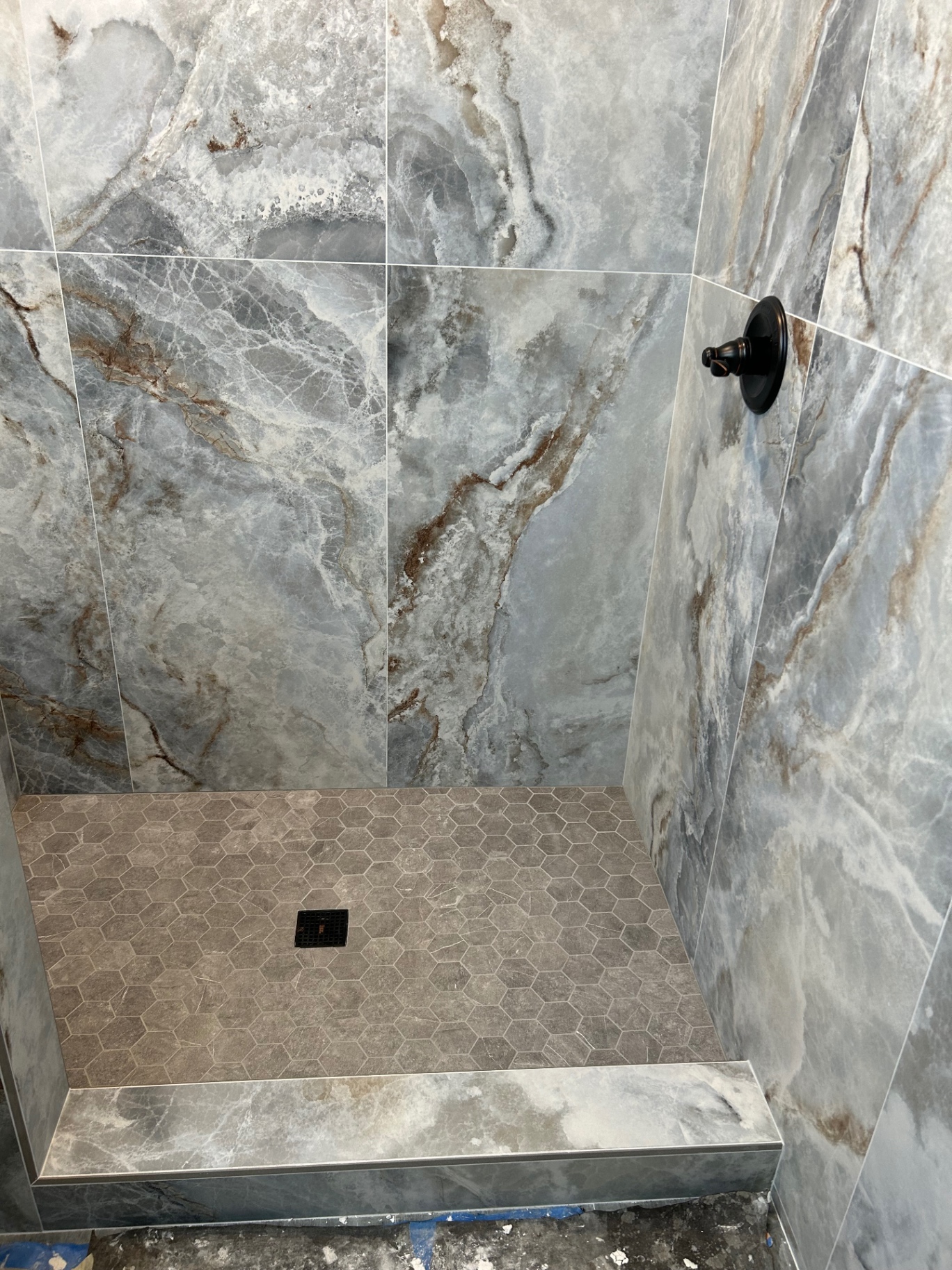 Onyx-look porcelain shower with hexagon mosaic floor and curb