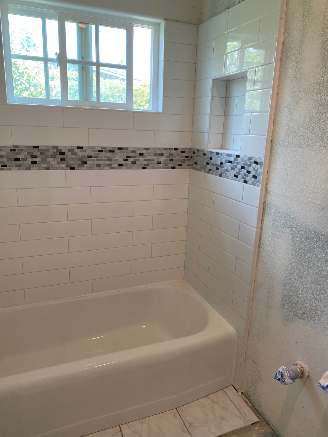 Tub surround with white subway tile and gray glass mosaic accent band with built-in niche