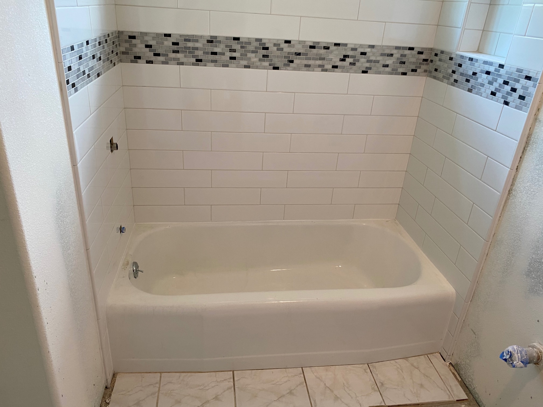 Wide view of white subway tub surround with gray and black glass mosaic border