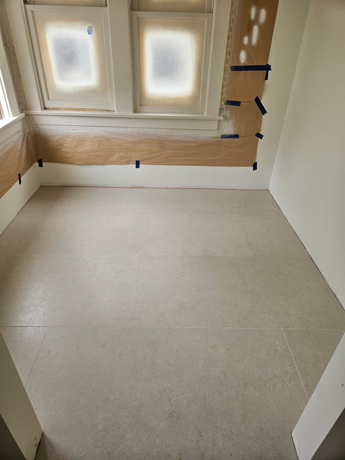 Large format limestone-look porcelain floor tile in bathroom by window
