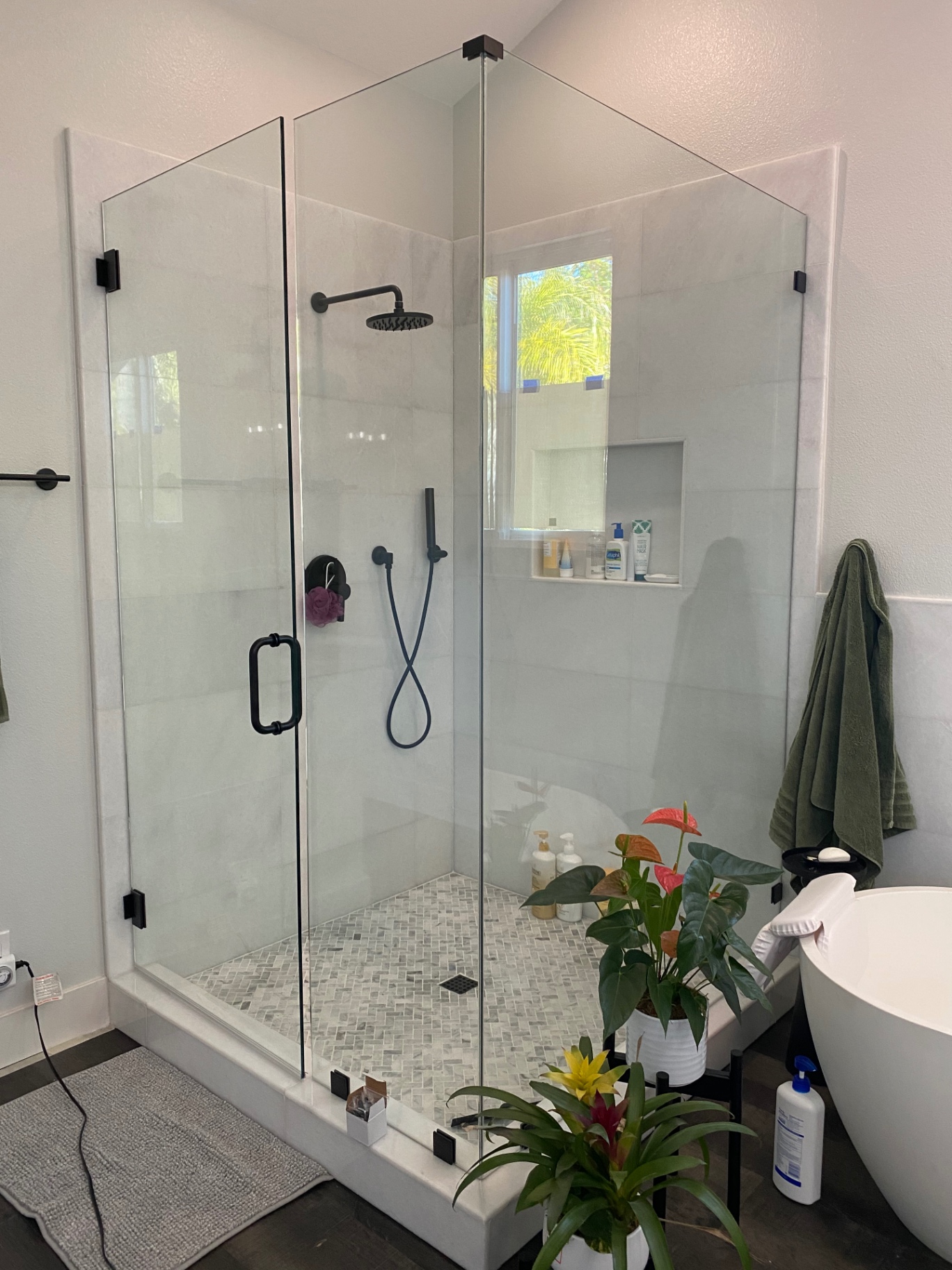 Frameless glass shower with matte black fixtures and light stone mosaic floor