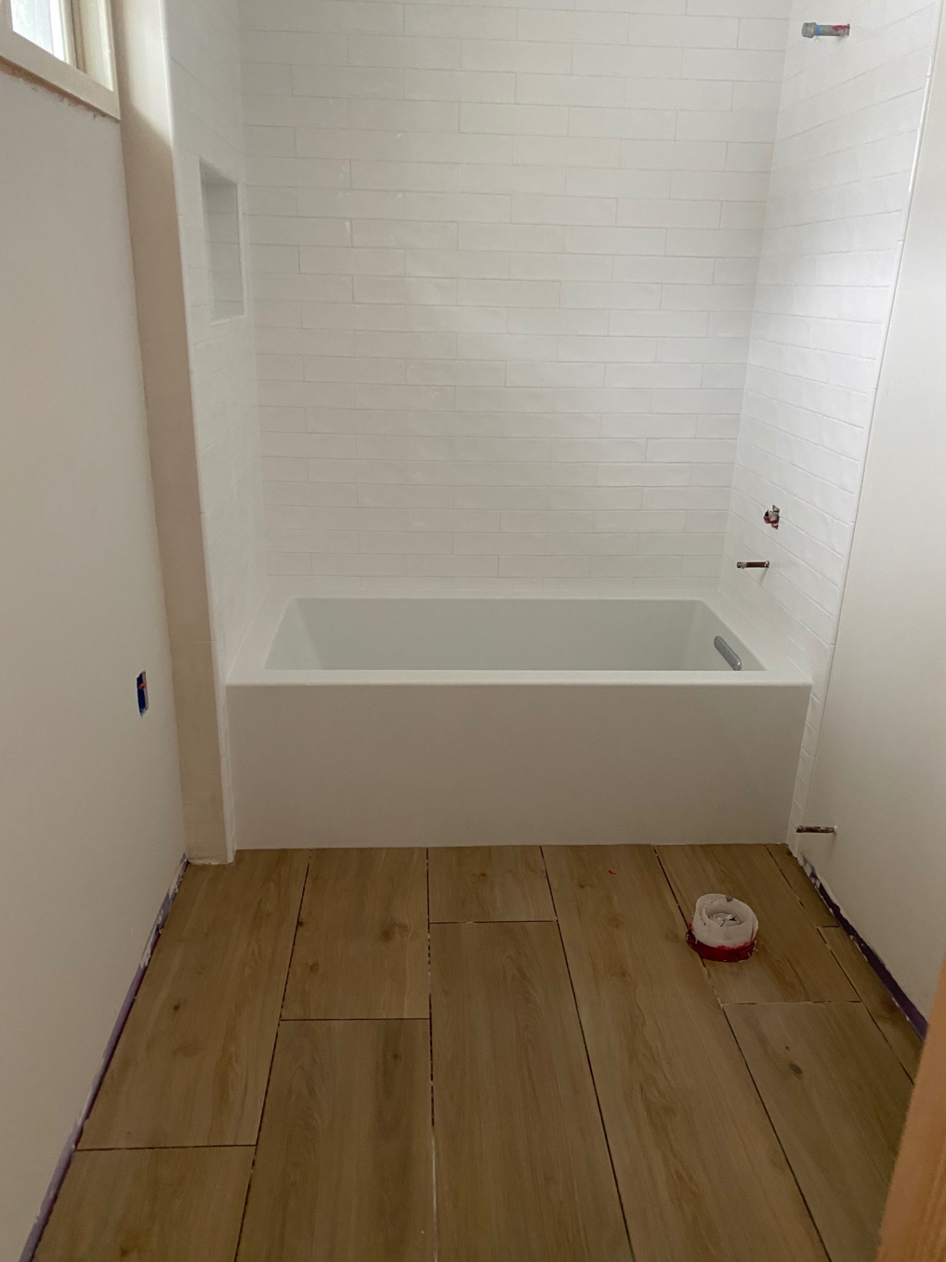 White stacked subway tile tub surround with niche and wood-look floor