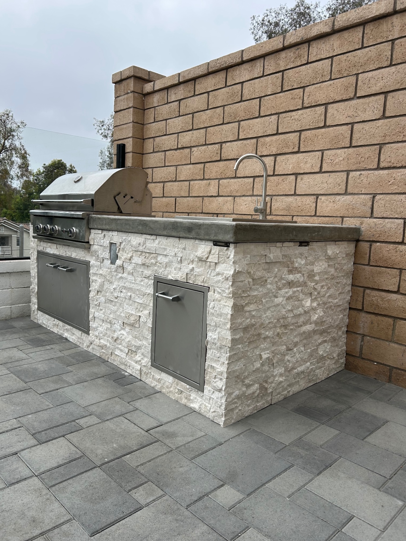 Angled view of outdoor kitchen with white ledger stone and stainless storage