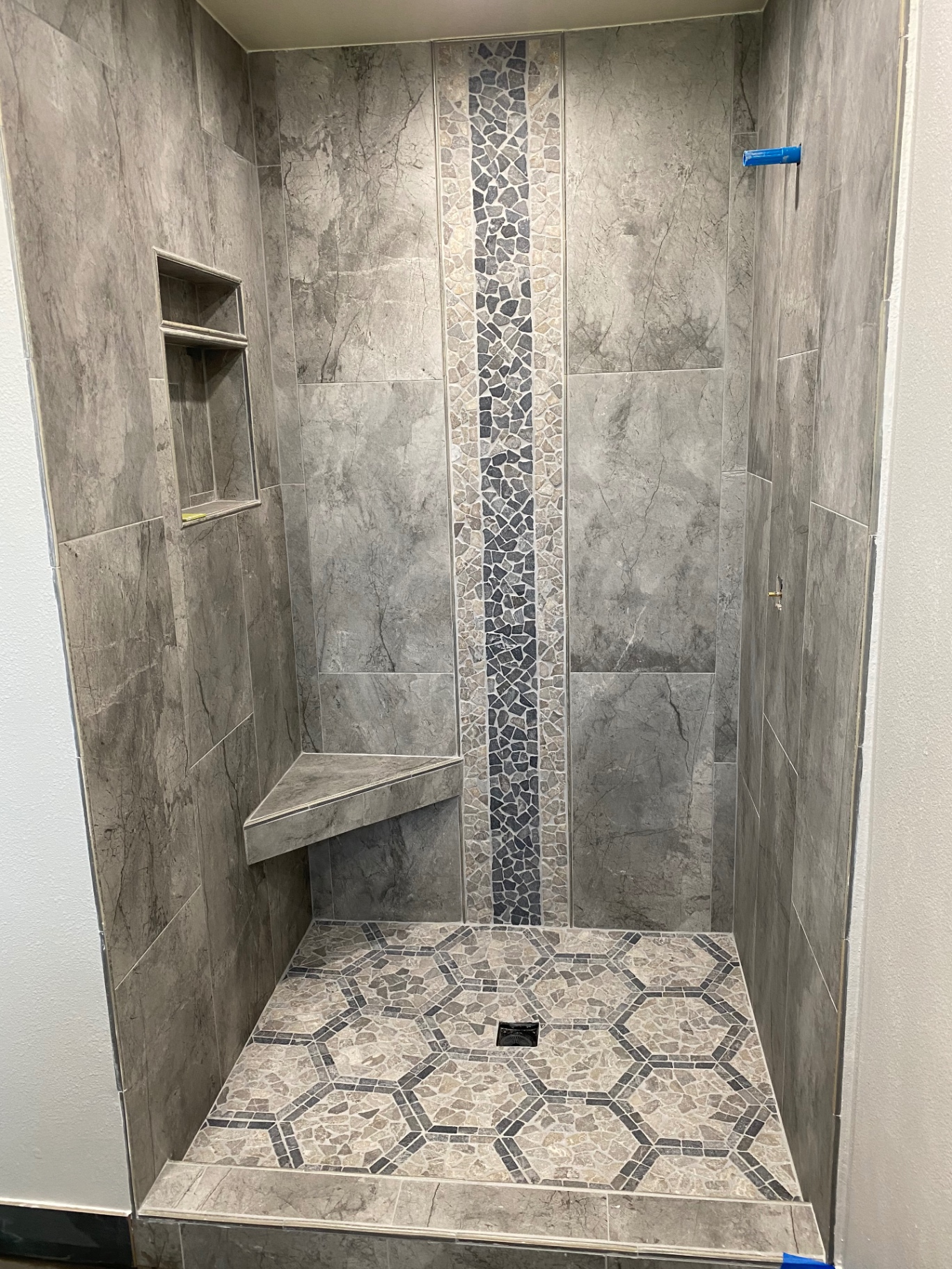 Gray marble shower with vertical black pebble mosaic stripe and hex stone floor