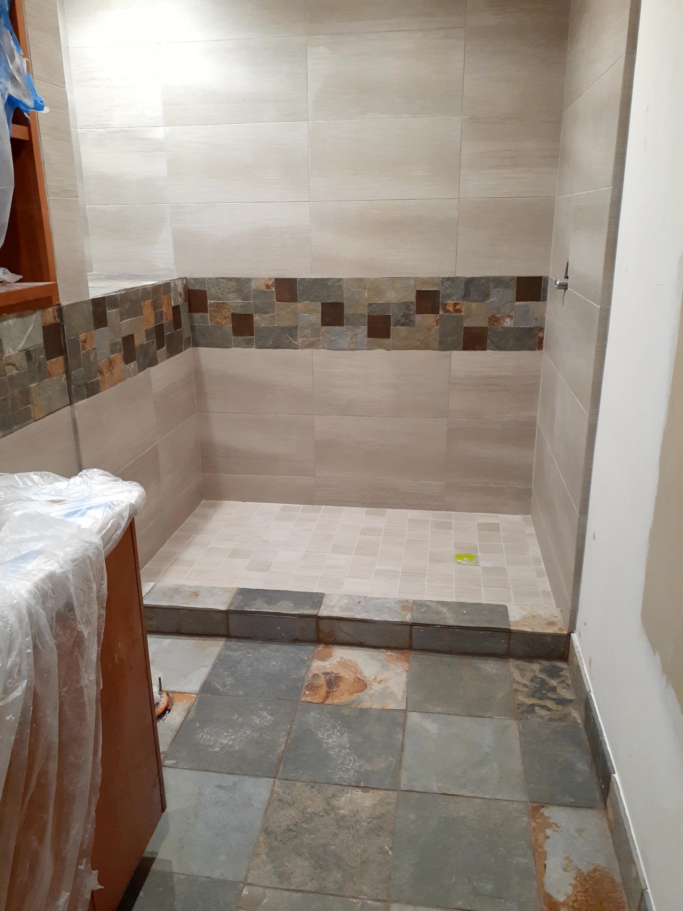 Earth-tone walk-in shower remodel with stone accent band and matching slate floor