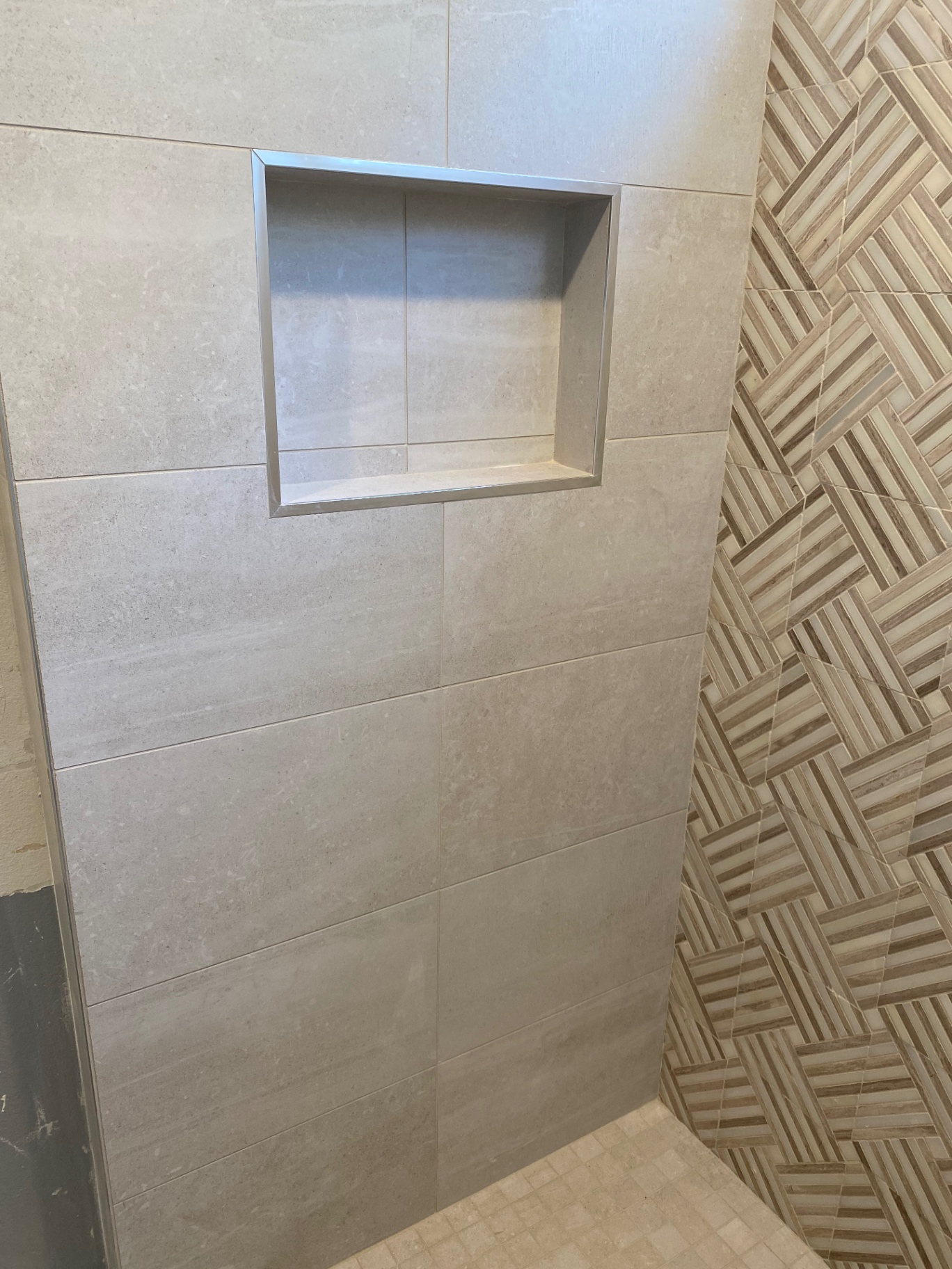 Shower niche detail in gray porcelain next to wood-look basketweave accent wall