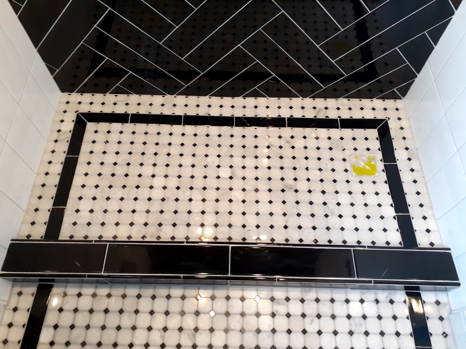 Close-up of black bordered shower pan with white octagon mosaic and black herringbone wall