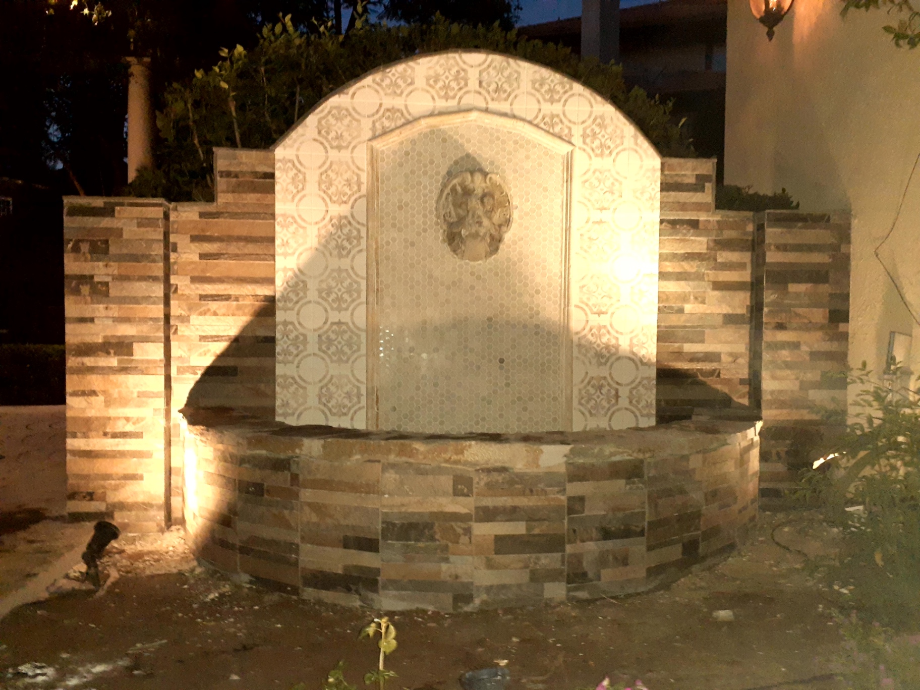 Outdoor stone fountain feature with decorative patterned tile at night