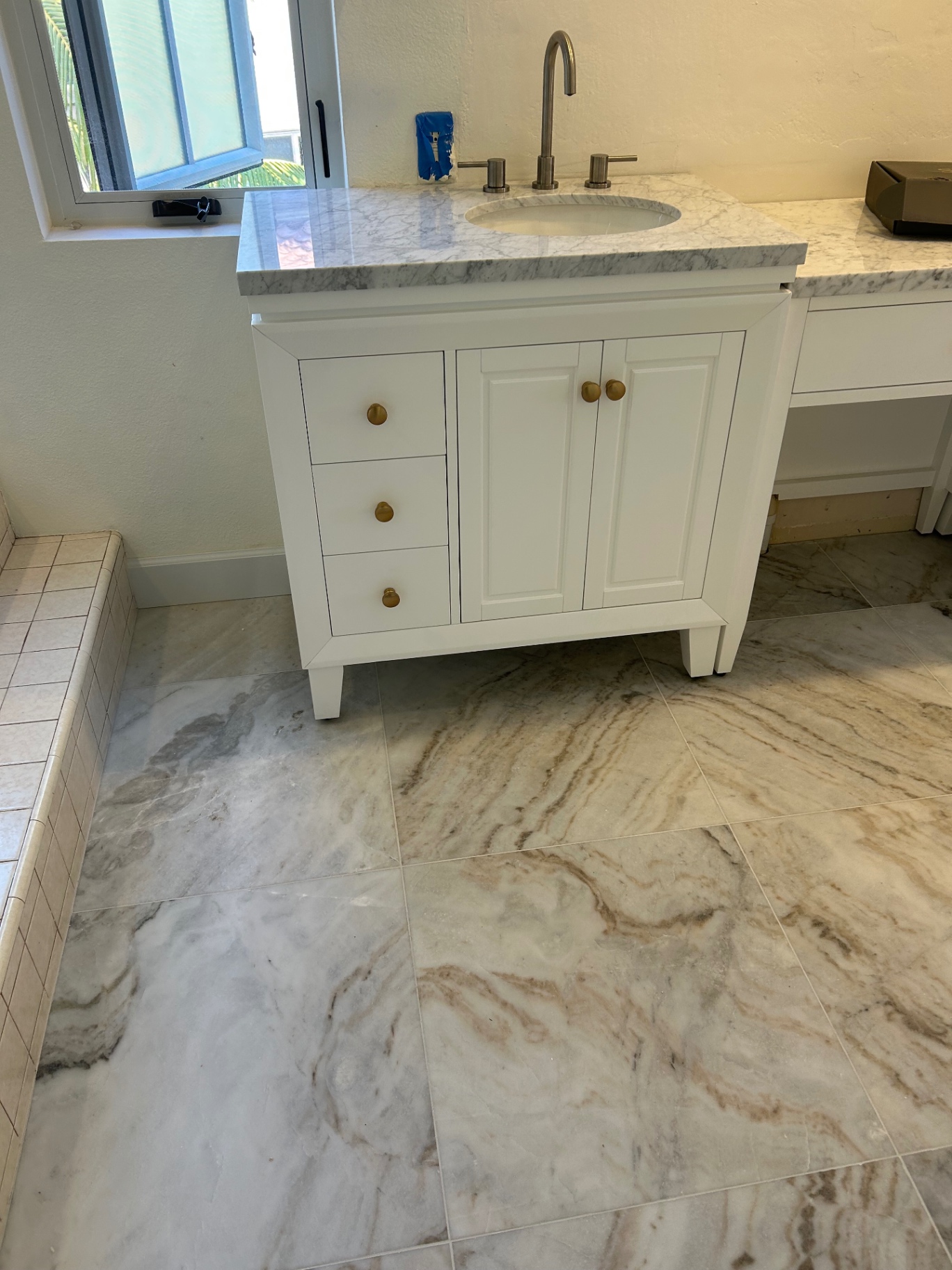 White shaker vanity with brass knobs and Carrara marble top on marble-look porcelain floor
