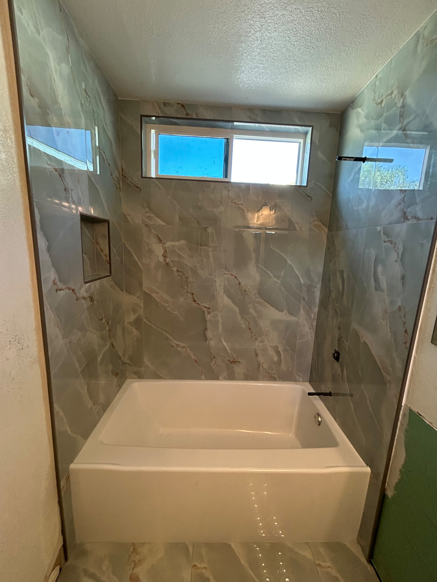Onyx-look large format porcelain tub surround with recessed niche and window trim