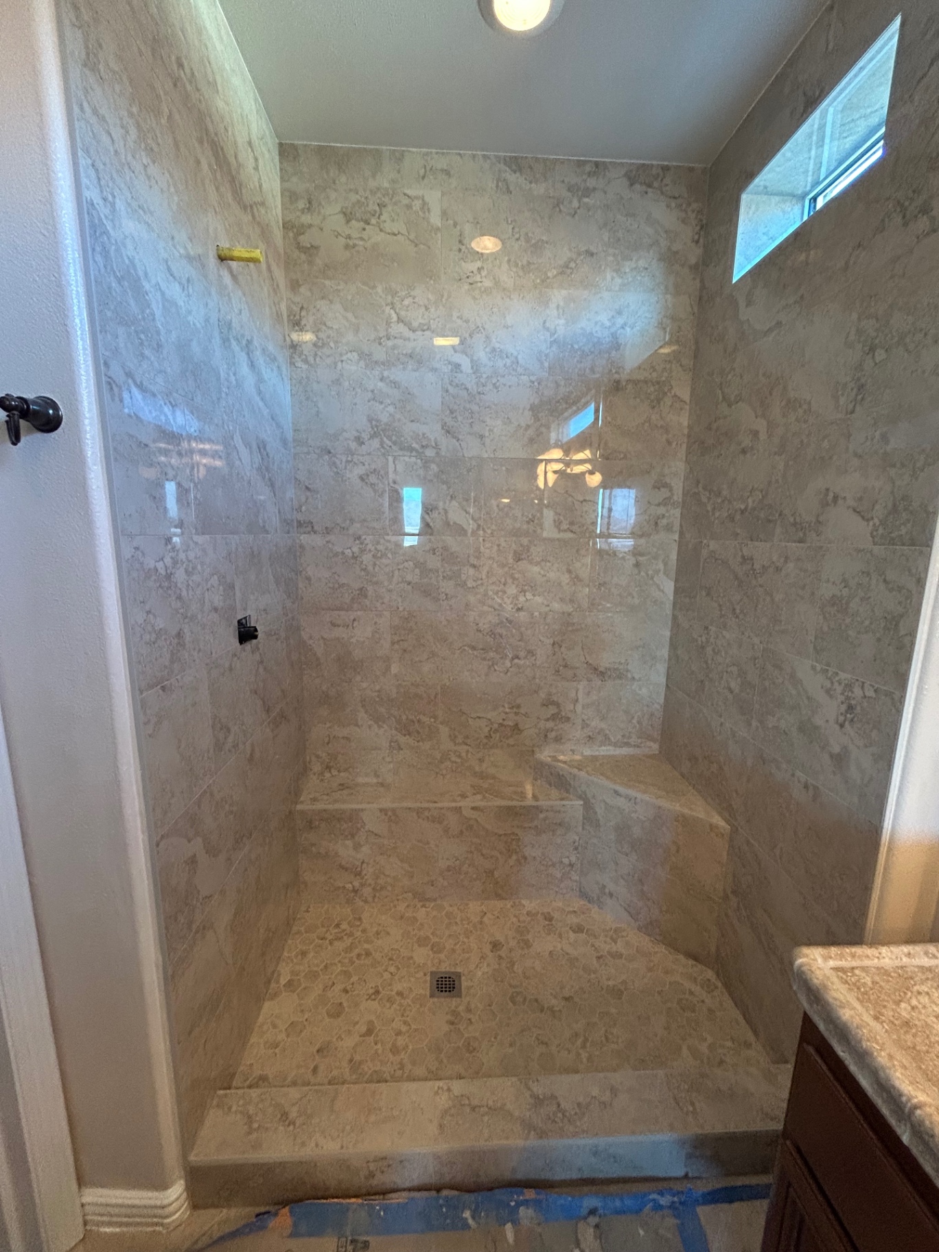 Travertine-look marble walk-in shower with bench and hex floor